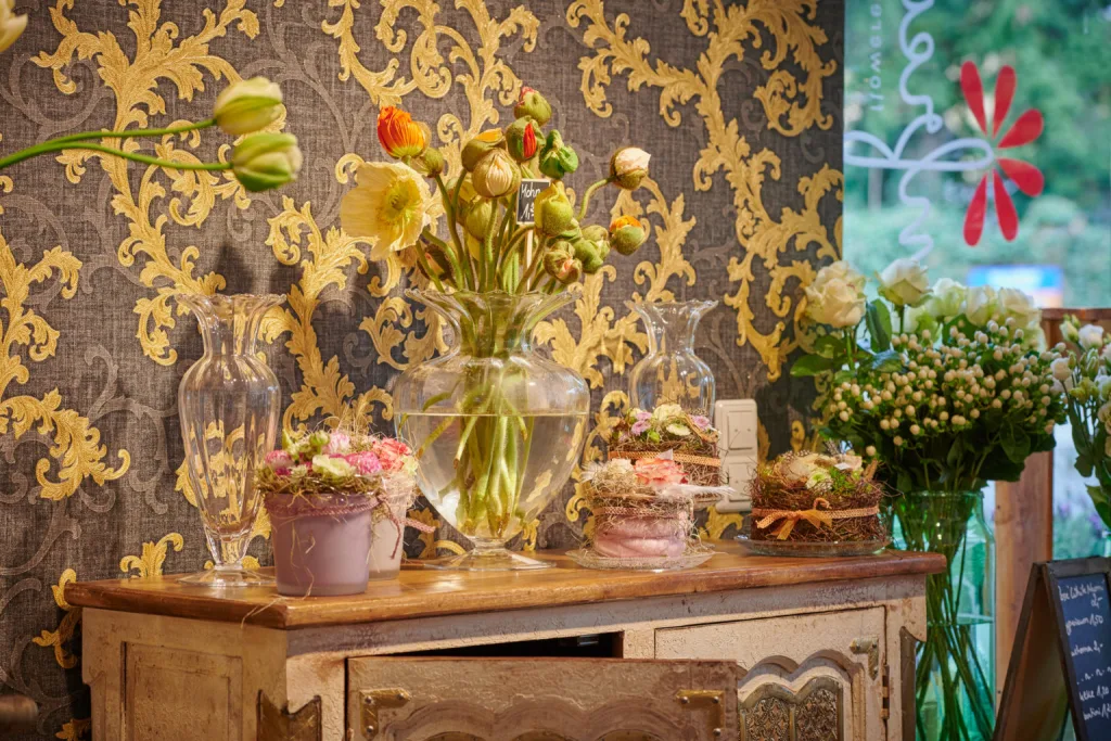 Antike Kommode mit Glasvasen, Mohnblumen und Blumentörtchen vor goldener Ornamenttapete
