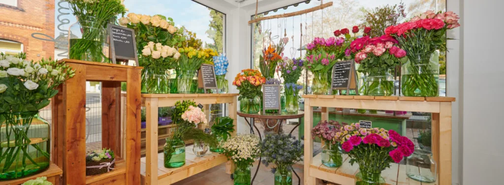 Schnittblumen in Glasvasen auf Holzregalen am Schaufenster, mit handgeschriebenen Preisschildern