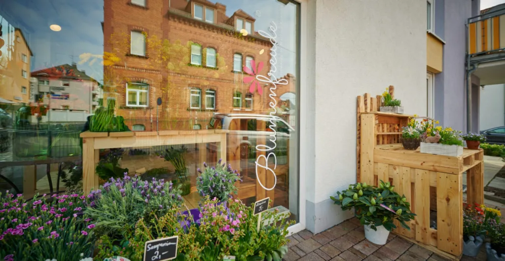 Außenansicht von Blumenfreude: Schaufenster mit Blumenfreude-Logo und bepflanzten Kisten davor