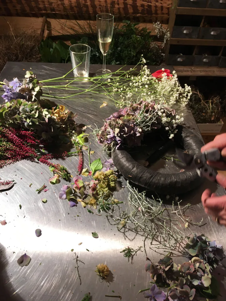 Arbeitstisch mit Hortensienblüten, Heidekraut und Schleierkraut, daneben ein Kranzrohling und eine Gartenschere