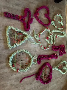 Neun im Workshop gefertigte Kränze und Herzen aus pinker und hellgrüner Wolle mit eingearbeiteten Trockenblumen