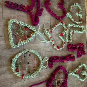 Neun im Workshop gefertigte Kr&auml;nze und Herzen aus pinker und hellgr&uuml;ner Wolle mit eingearbeiteten Trockenblumen