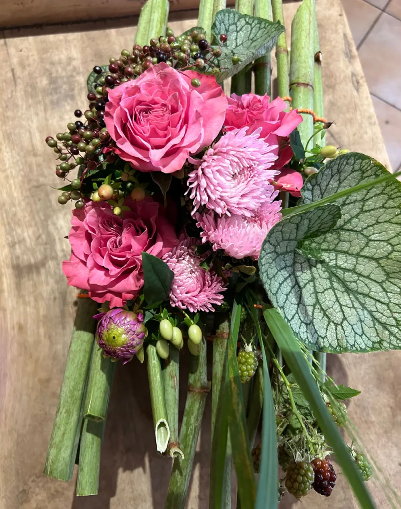 Strauß aus pinken Rosen, Chrysanthemen, Brombeerranken und Beerenzweigen auf einem Holztisch