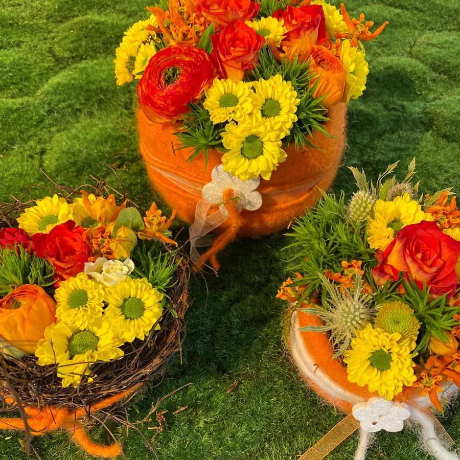 Blumentörtchen mit orangen Rosen, Ranunkeln und gelben Chrysanthemen auf einer Moosfläche