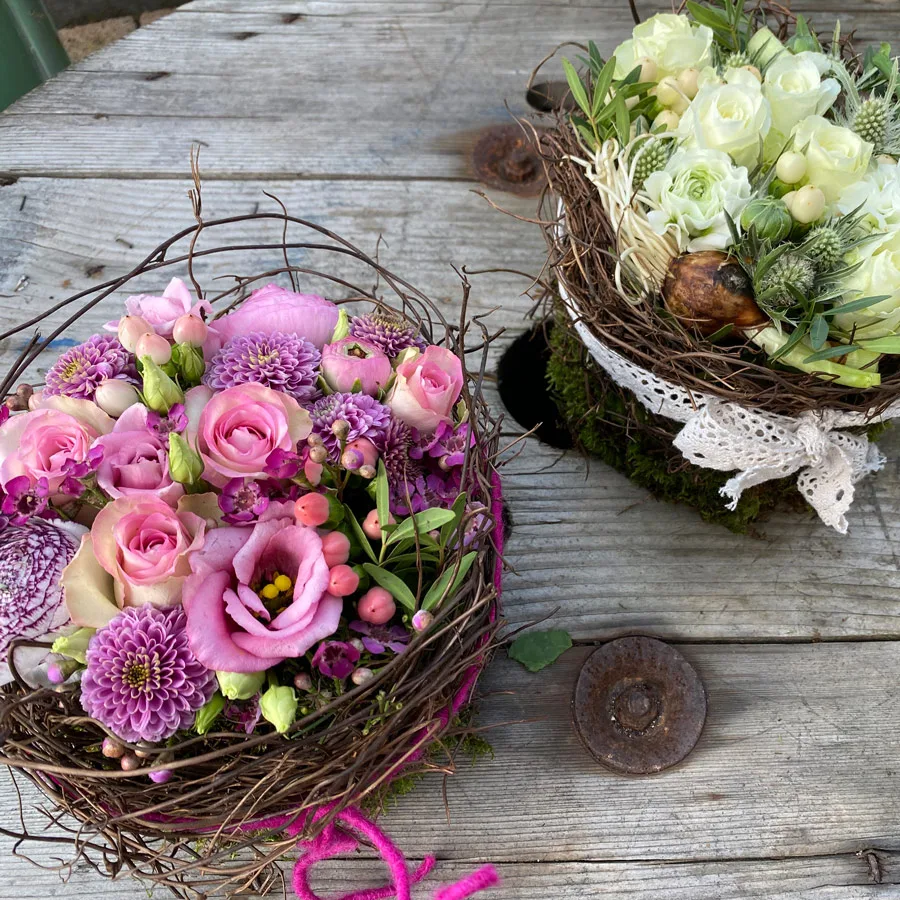 Zwei Blumentörtchen in Zweignestern mit rosa Rosen und mit weißen Rosen auf verwittertem Holz