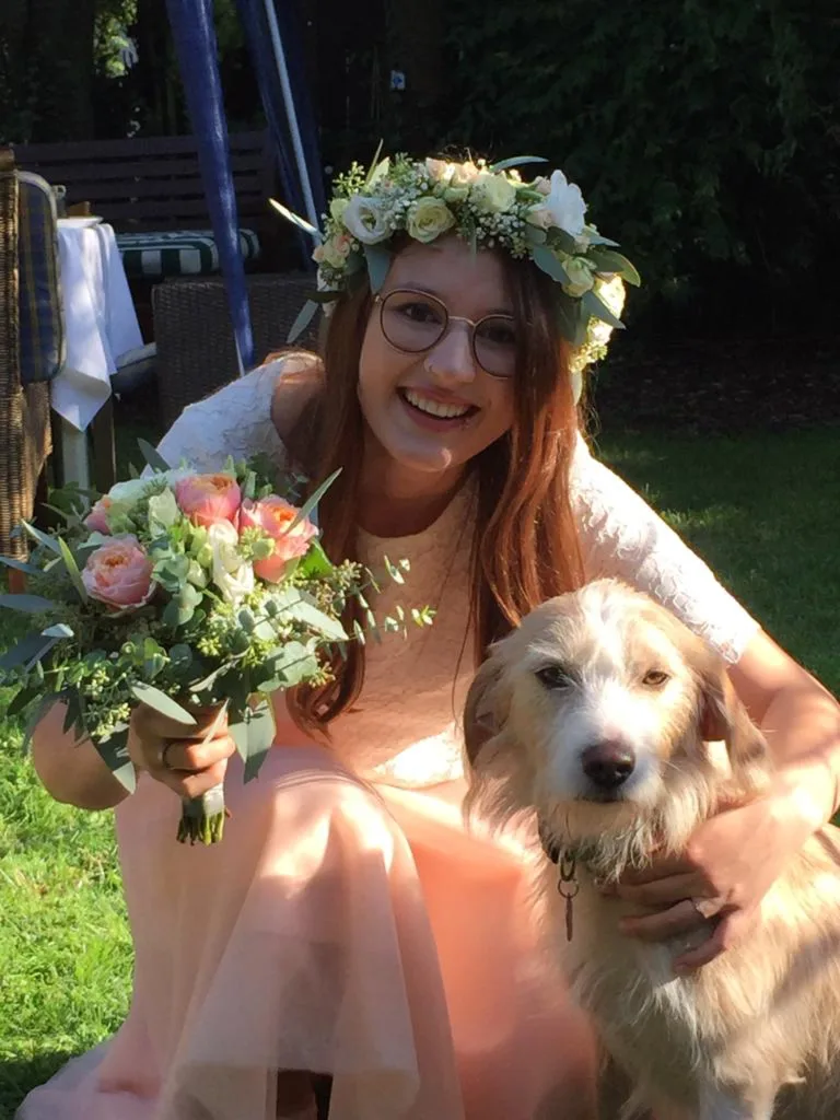 Junge Frau mit Blumenkranz im Haar und pastellfarbenem Strauß, neben ihr ein Golden Retriever