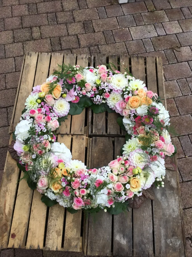 Runder Trauerkranz mit rosa und weißen Nelken, Rosen und Chrysanthemen auf einer Holzpalette