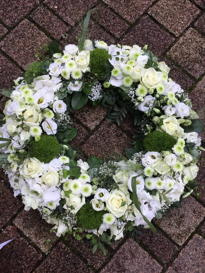 Runder Trauerkranz mit weißen Rosen, Chrysanthemen und Moos auf einem Pflasterweg