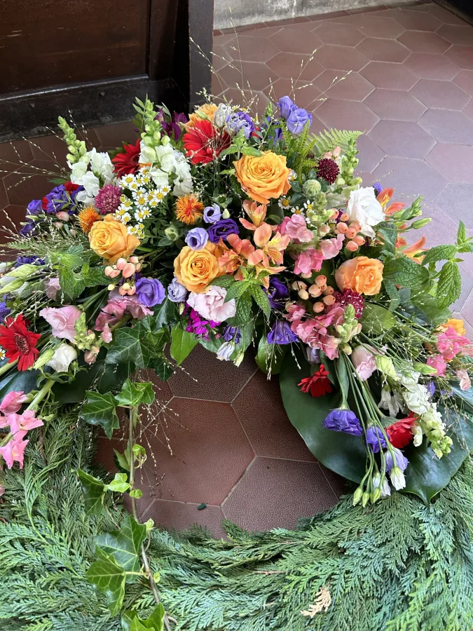 Trauerkranz aus Tannengrün mit orangen Rosen sowie pinken und violetten Blüten