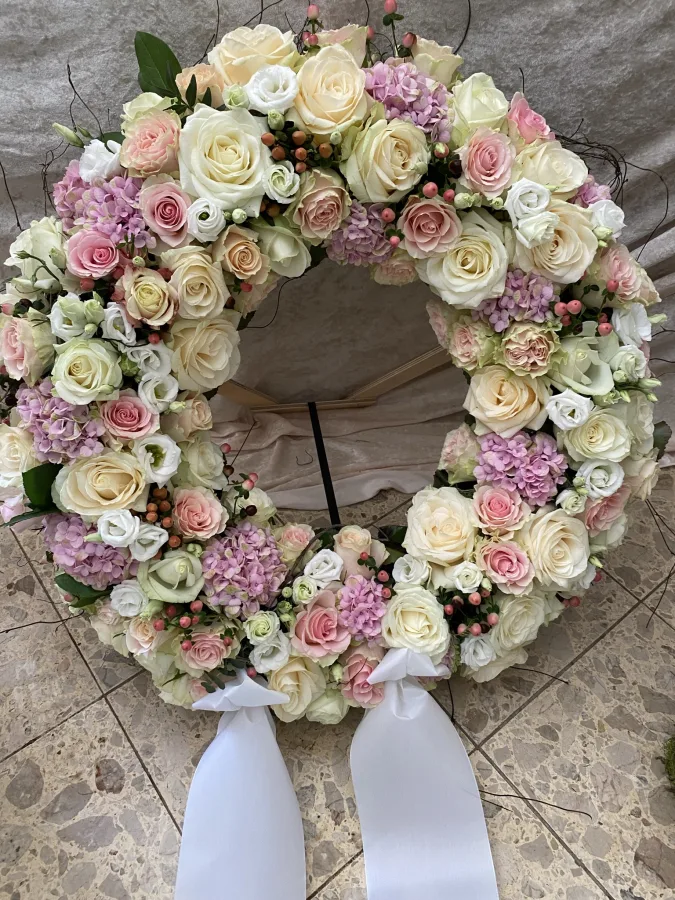 Runder Trauerkranz aus cremefarbenen und rosa Rosen mit weißen Schleifenbändern