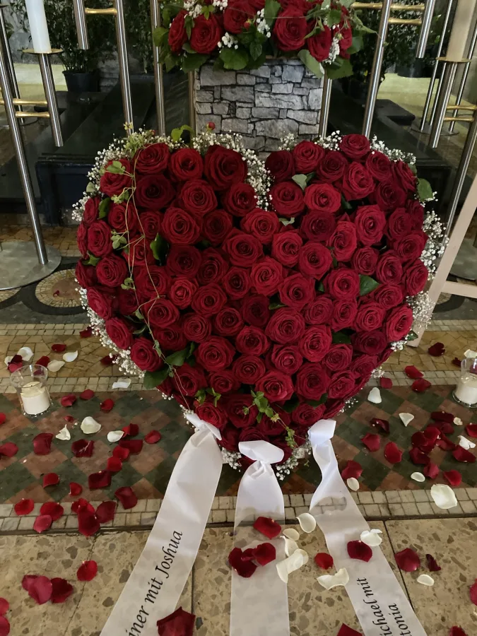 Herzförmiges Trauergesteck dicht gesteckt mit roten Rosen und weißen Schleifen