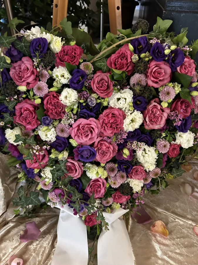 Herzförmiges Trauergesteck mit pinken Rosen, weißen Lisianthus und violetten Blüten