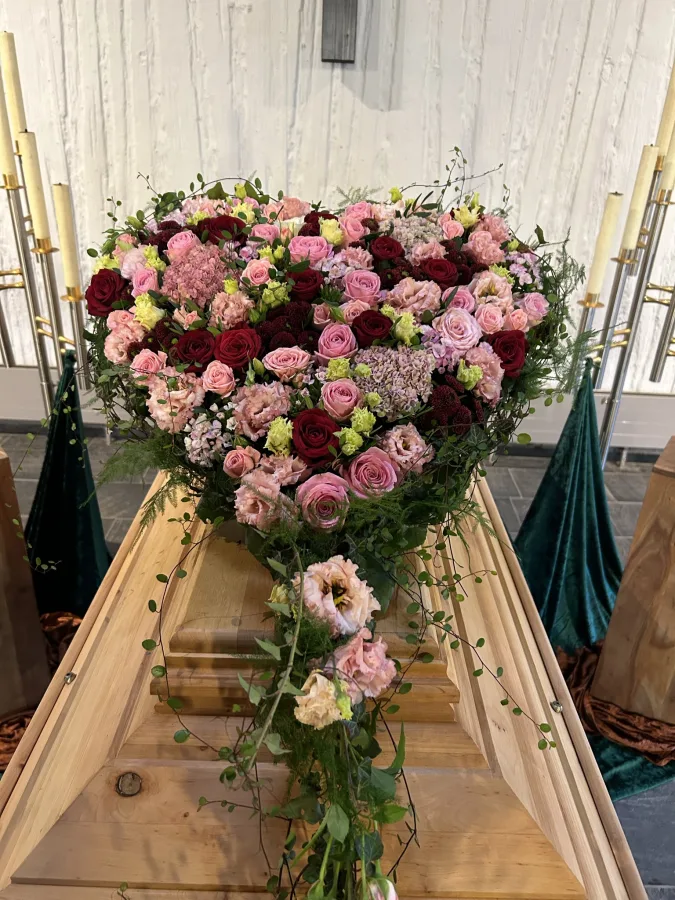 Herzförmiges Trauergesteck mit rosa und bordeauxfarbenen Rosen auf einem Holzsarg