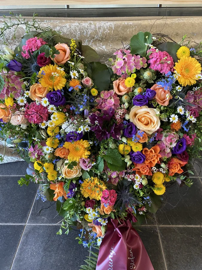 Herzförmiges Trauergesteck mit bunten Sommerblumen auf einem Ständer