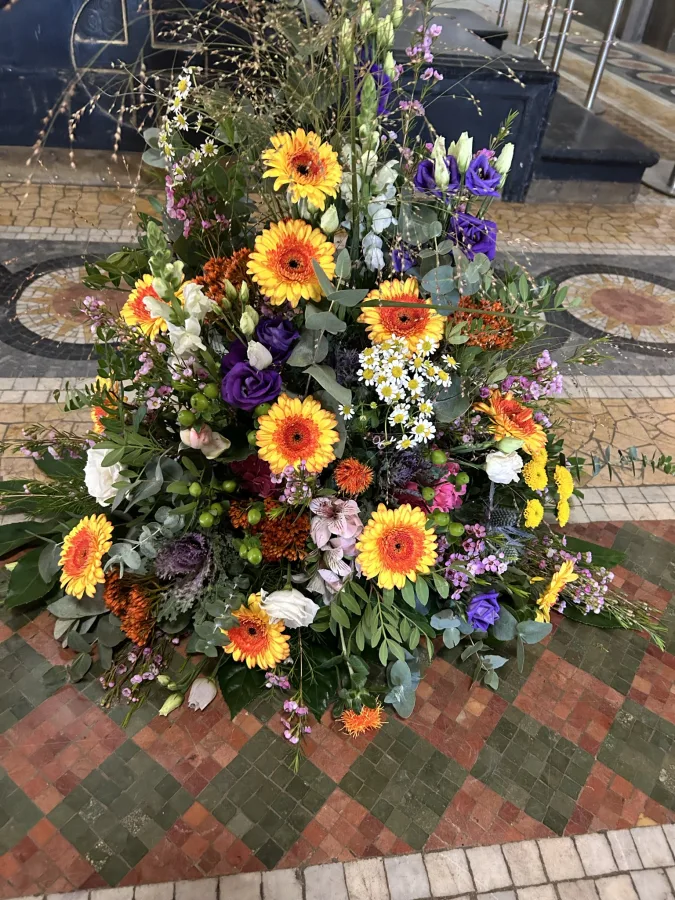 Trauergesteck mit orangen Gerbera sowie gelben und violetten Blüten in einer Kapelle