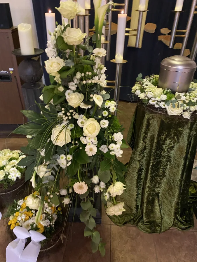 Urne auf grünem Samtpodest mit weißem Blumenschmuck und Kerzenleuchtern