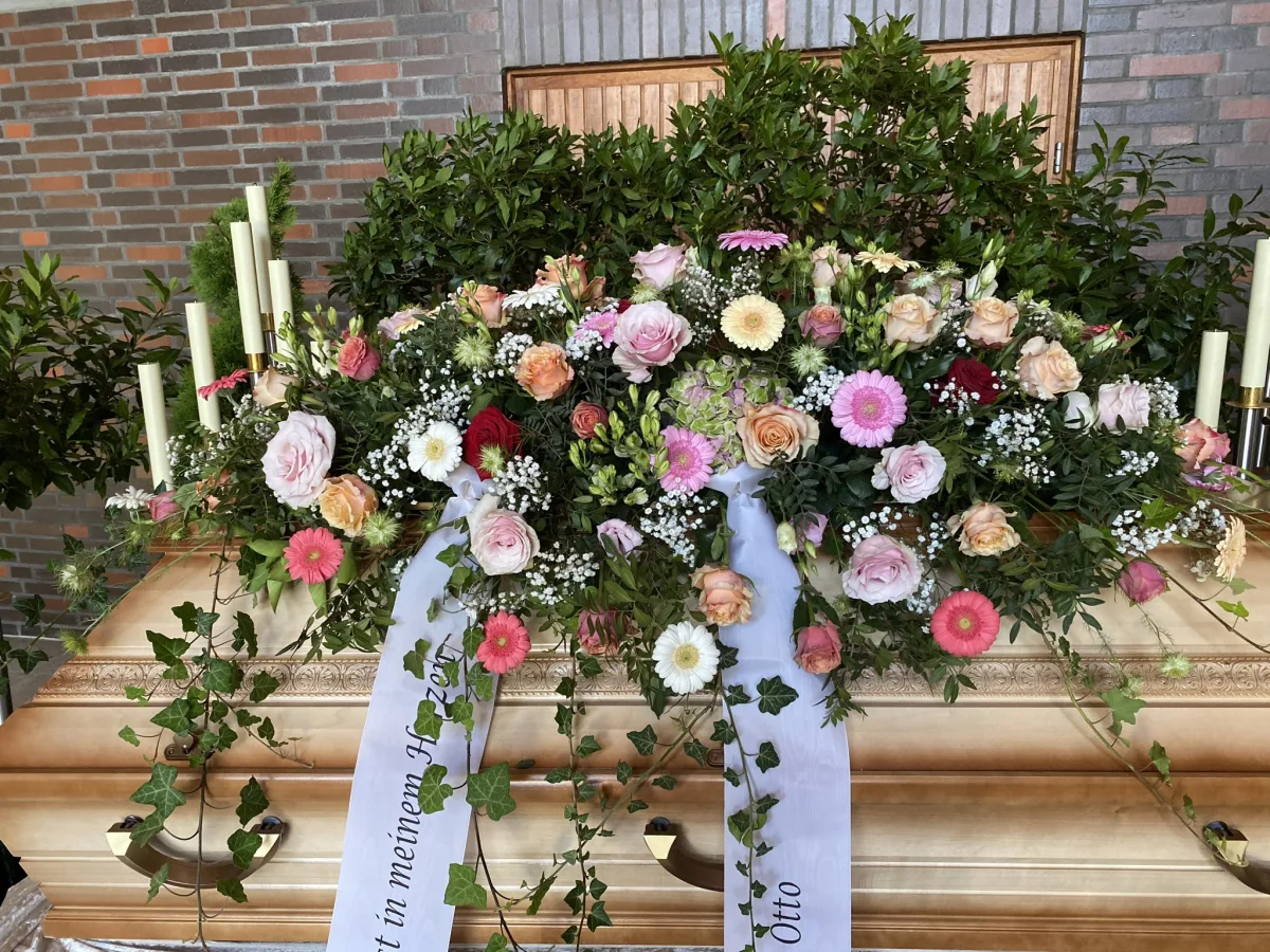 Sargbouquet mit rosa und weißen Rosen, Nelken und beschrifteten Trauerschleifen