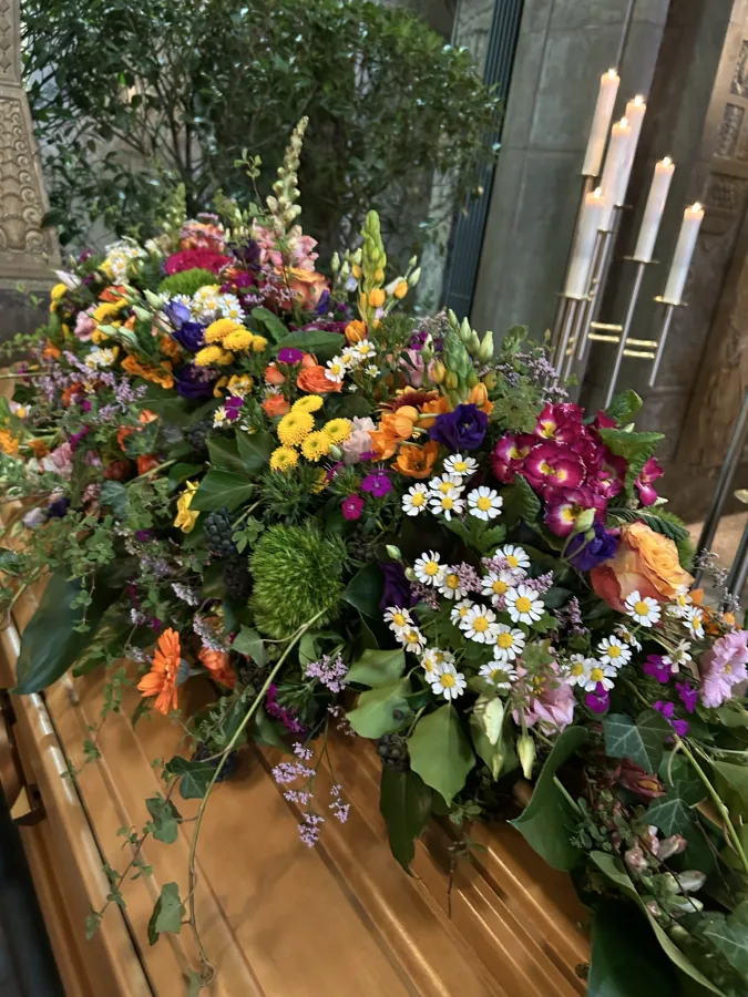 Sargbouquet mit gelben, violetten und weißen Sommerblumen auf einem Holzsarg