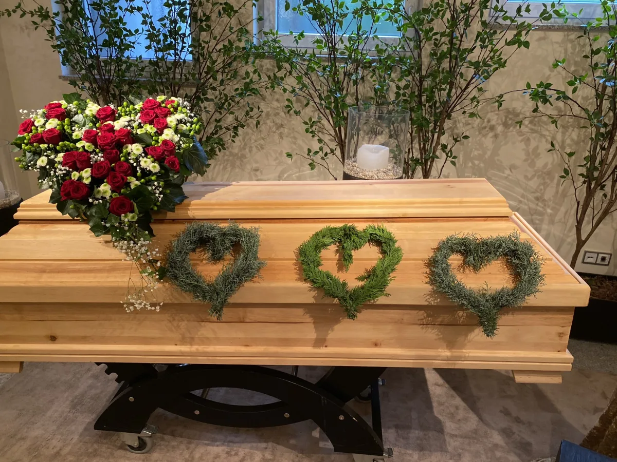 Holzsarg mit rotem Blumenschmuck und drei kleinen Herzen aus Efeu