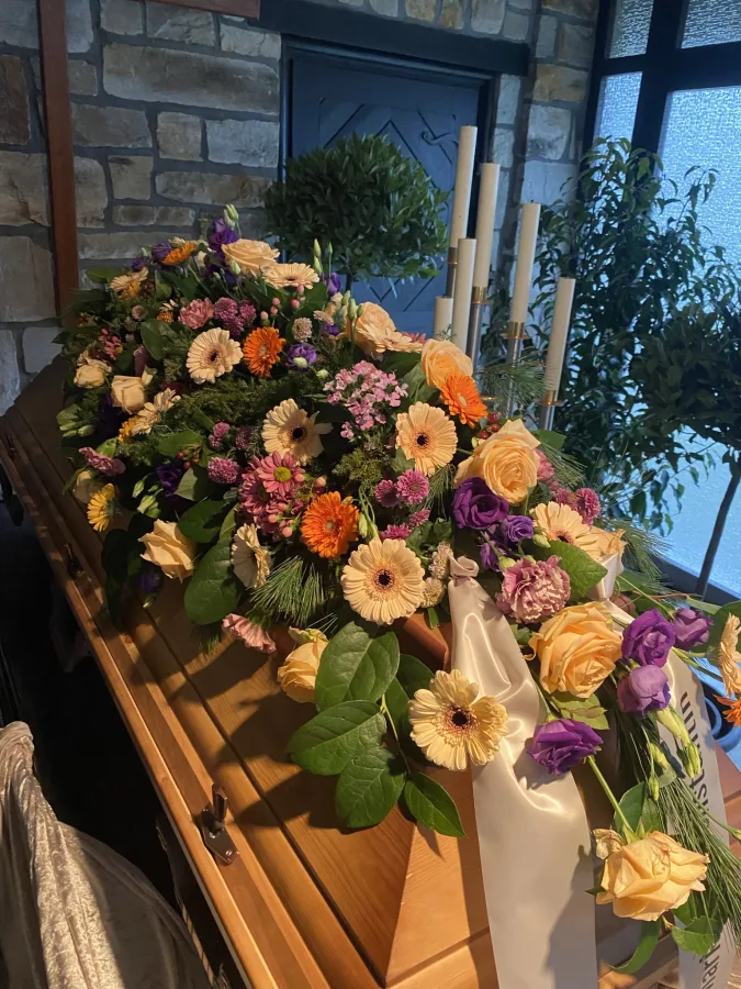 Sargbouquet mit orangen Rosen und Gerbera auf einem Holzsarg