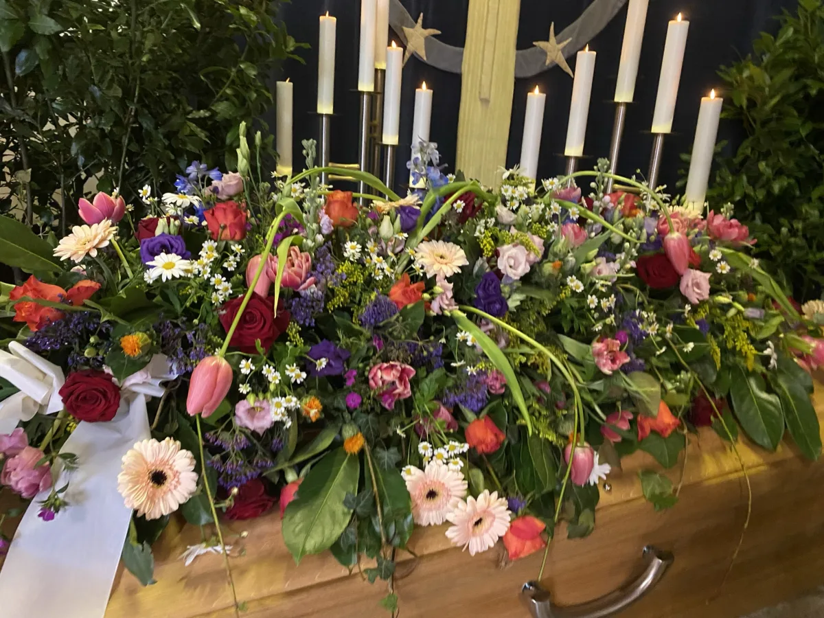 Sargbouquet mit Tulpen, Gerbera und bunten Frühlingsblumen auf einem weißen Sarg