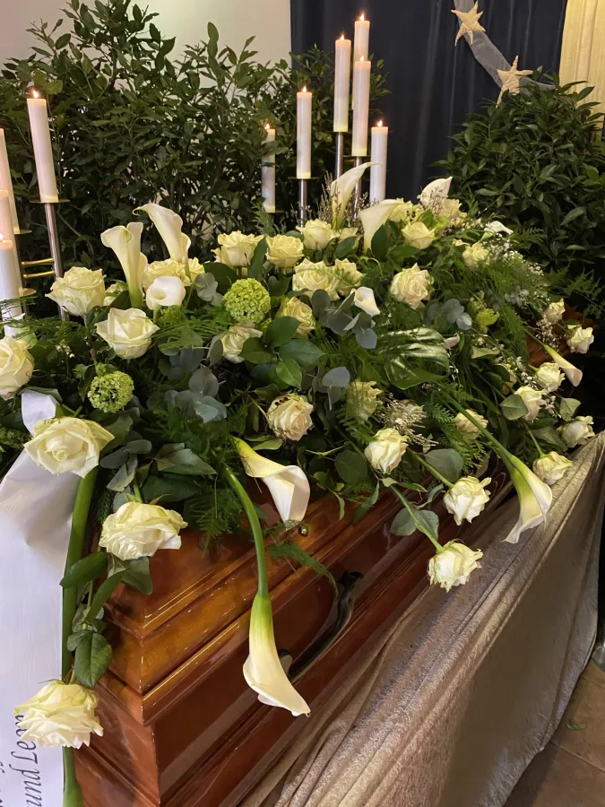 Sargbouquet mit weißen Callas, Rosen und Eukalyptus vor hohen Kerzenleuchtern
