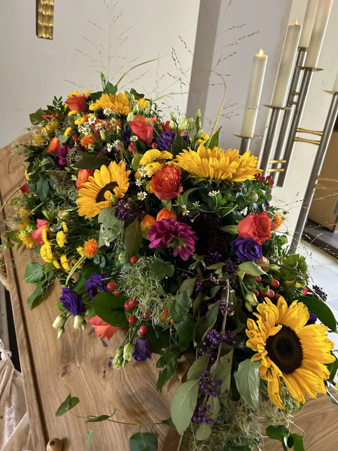 Sargbouquet mit Sonnenblumen sowie roten und violetten Blüten auf einem Holzsarg