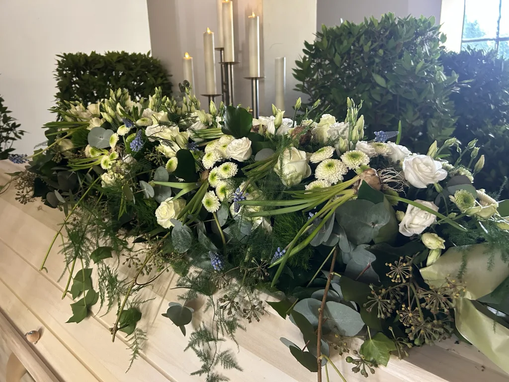 Sargbouquet mit weißen Rosen, Lisianthus und Eukalyptus auf einem hellen Sarg