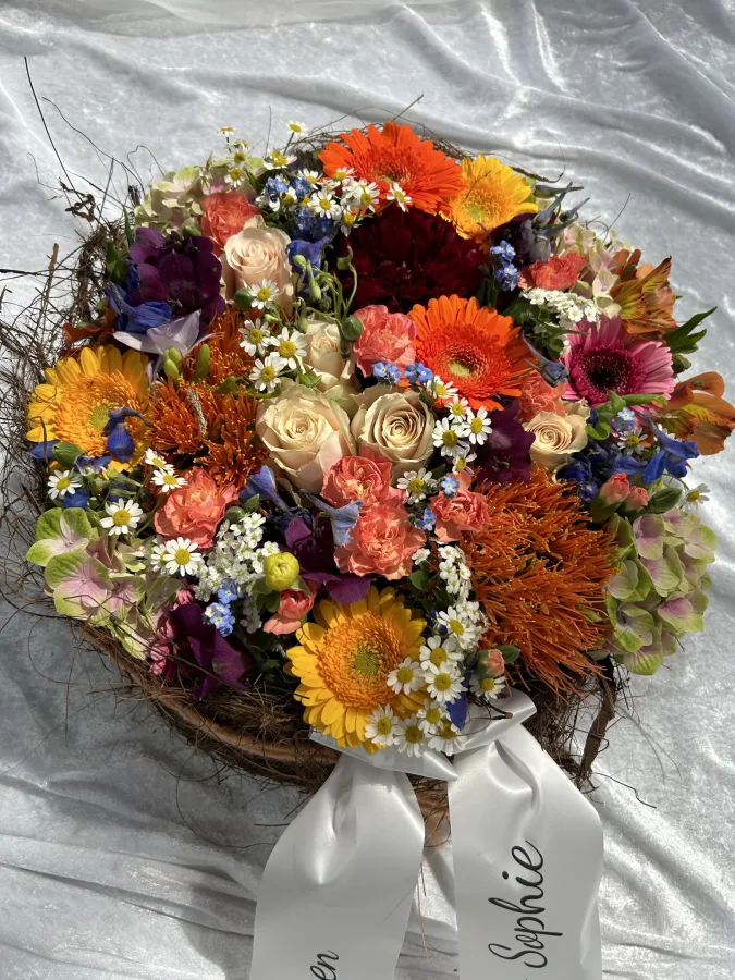 Runder Trauerstrauß mit orangen Gerbera, cremefarbenen Rosen und beschrifteter Schleife