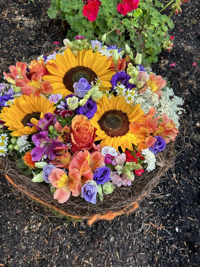 Rundes Gesteck mit Sonnenblumen und bunten Sommerblumen auf einem Grab