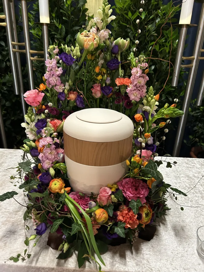 Helle Urne umgeben von einem Kranz aus rosa, orangen und violetten Blüten