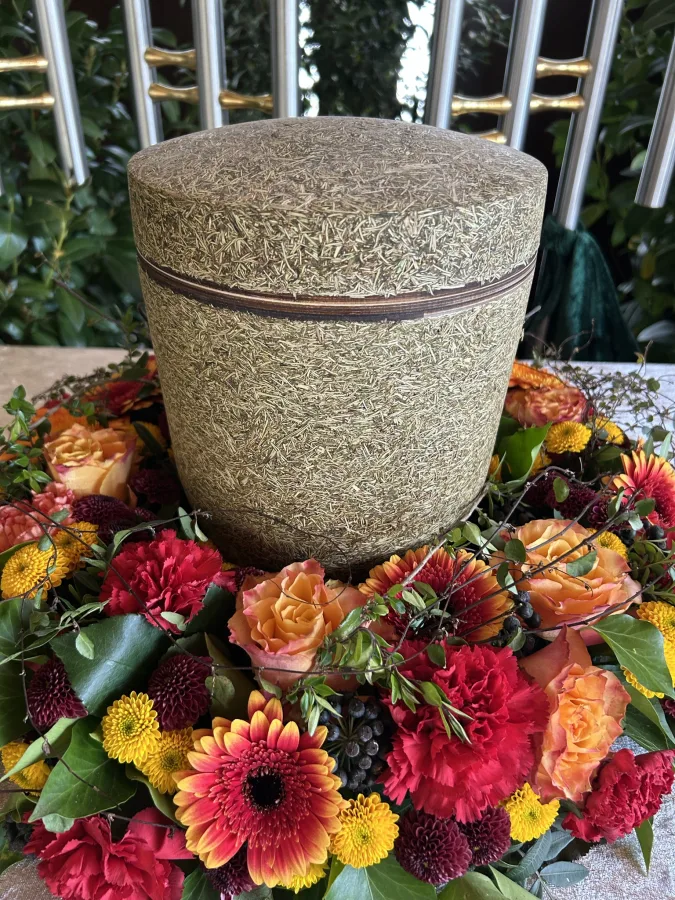 Steinurne mit einem Kranz aus roten und orangen Gerbera und Dahlien