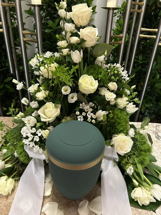 Dunkelgrüne Urne mit weißen Rosen, Lisianthus und weißer Schleife
