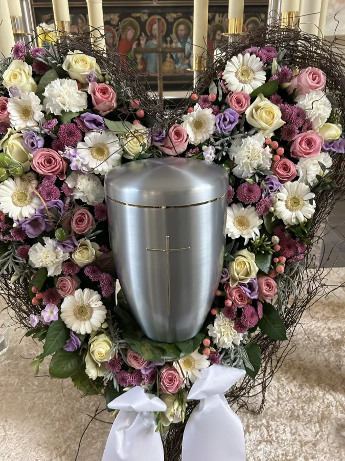 Silberne Urne in einem herzförmigen Kranz aus rosa und weißen Rosen