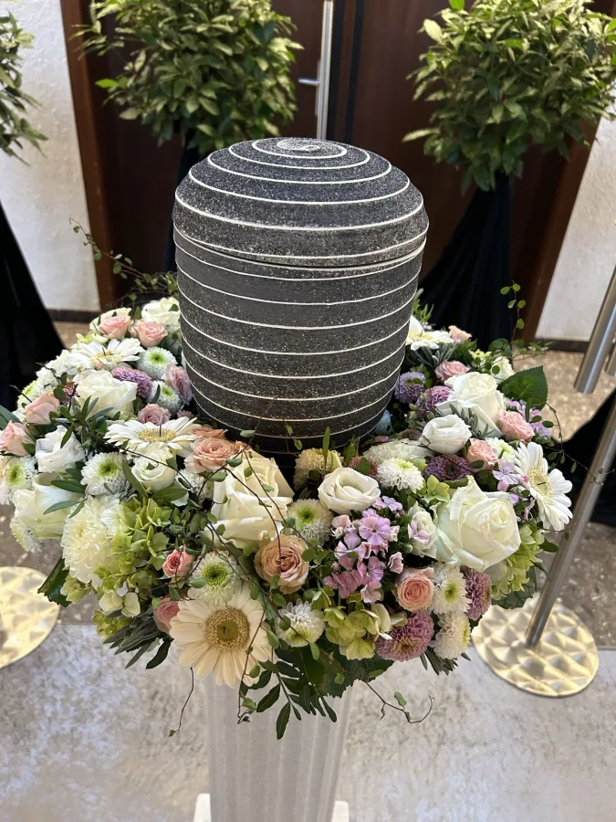 Grau gemusterte Urne auf einer Säule mit weißen Rosen und Chrysanthemen