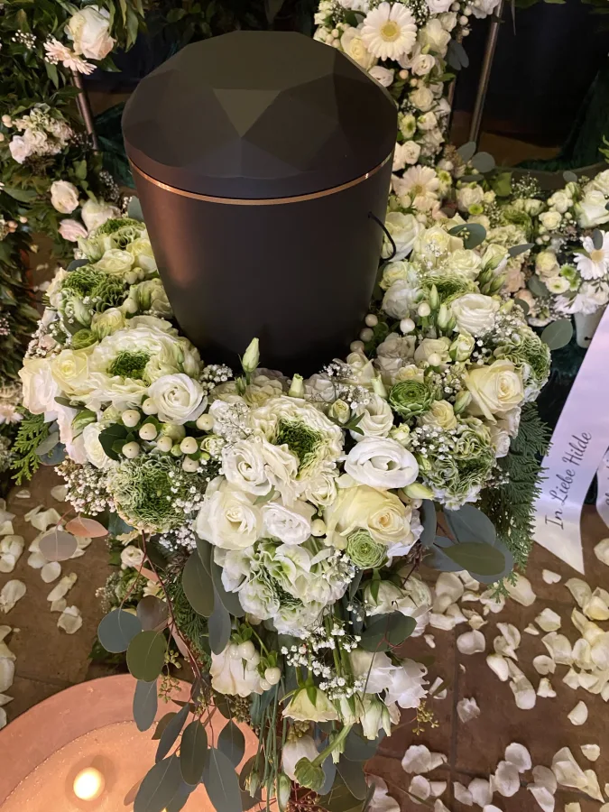 Dunkle Urne umgeben von weißen Rosen, Chrysanthemen und Schleierkraut
