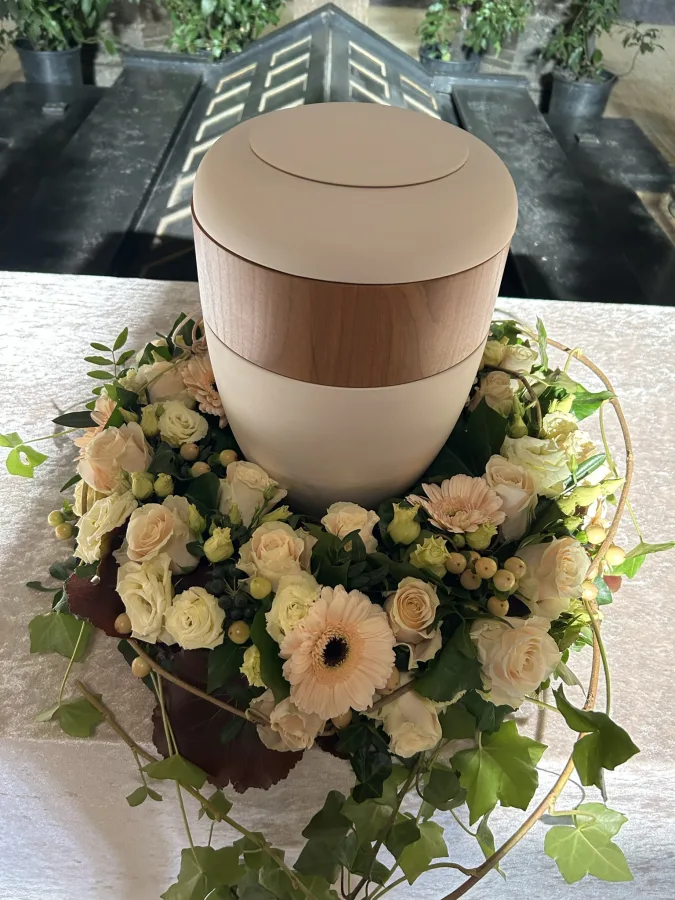 Beigefarbene Urne mit cremefarbenen Rosen, weißen Anemonen und Efeu
