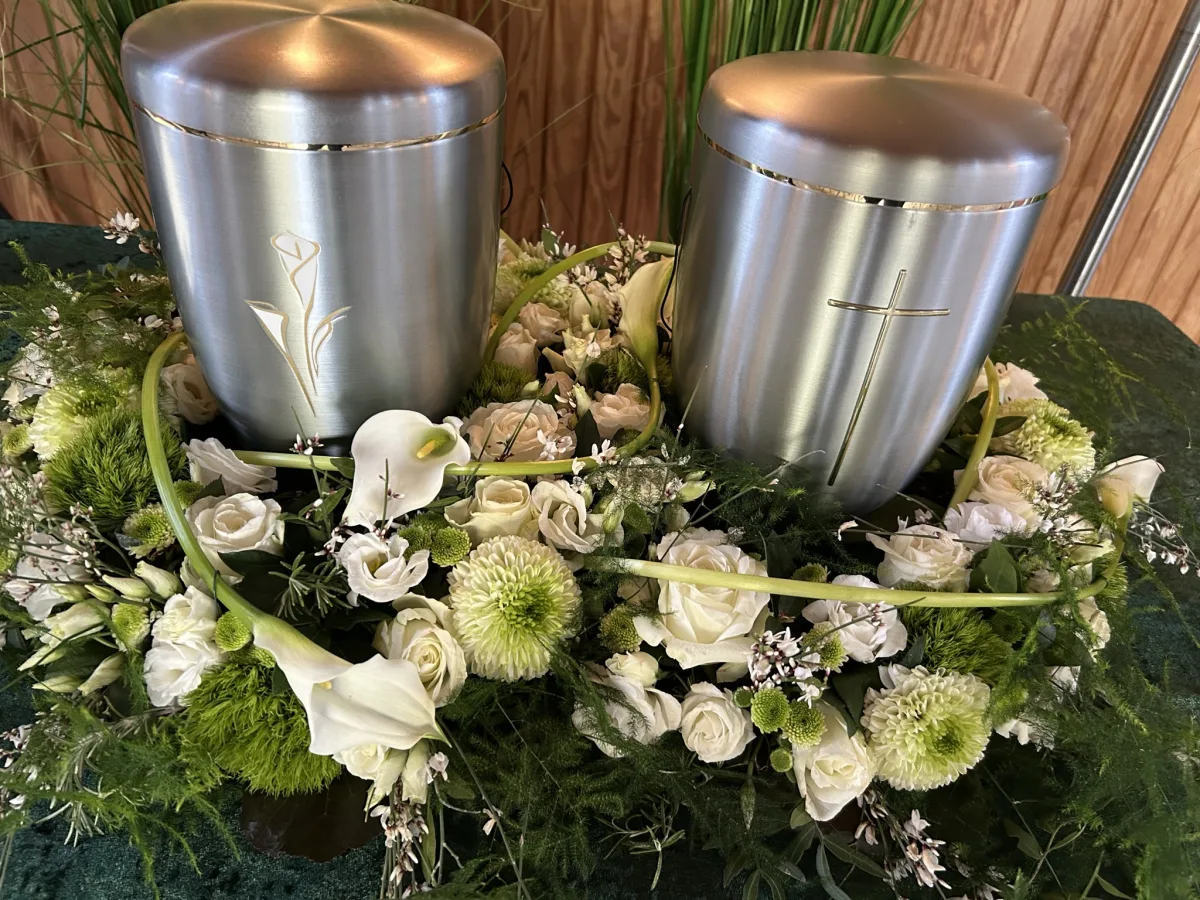Zwei silberne Urnen in einem gemeinsamen Gesteck aus weißen Callas und Rosen