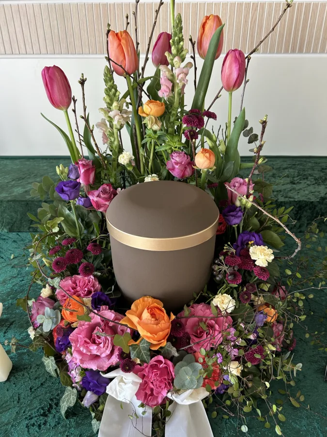 Dunkle Urne umgeben von Tulpen, Rosen und bunten Frühlingsblumen