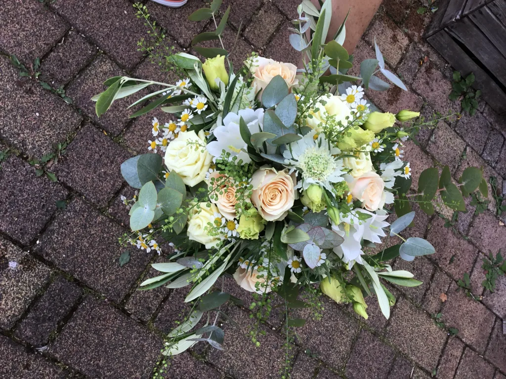 Brautstrauß mit weißen und cremefarbenen Rosen, Eukalyptus und Olivenzweigen auf Pflastersteinen