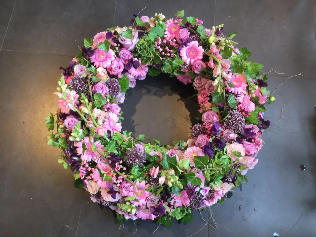 Runder Trauerkranz mit rosa und violetten Blüten und viel frischem Grün