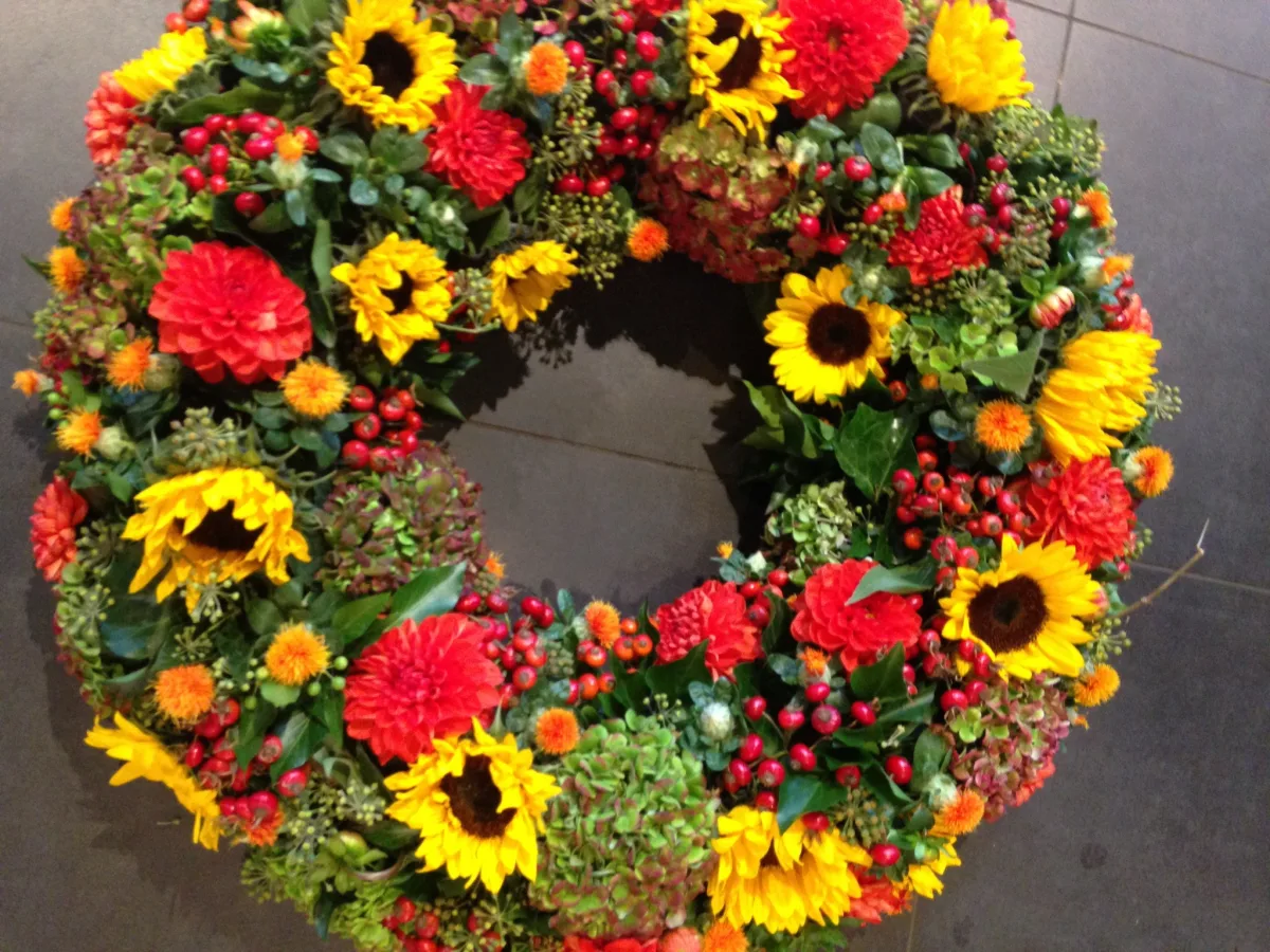 Runder Trauerkranz mit Sonnenblumen, roten Dahlien und Hagebutten