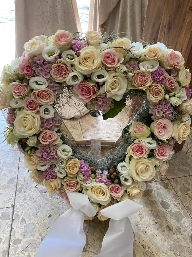 Herzförmiger Trauerkranz aus cremefarbenen und rosa Rosen mit weißen Schleifen