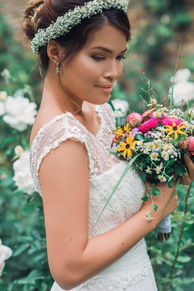 Braut mit Blumenkranz im Haar hält einen bunten Brautstrauß mit gelben und pinken Blüten