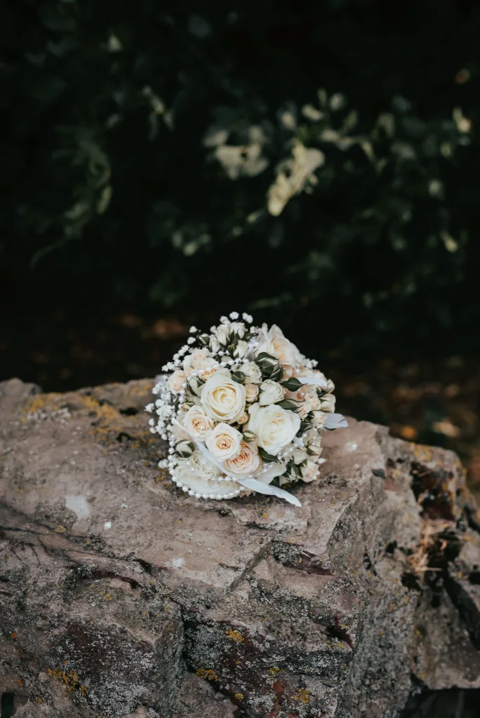Brautstrauß aus weißen Rosen und Schleierkraut auf einem bemoosten Stein