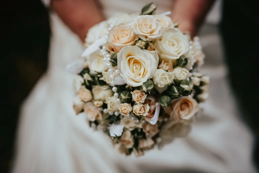Braut hält einen Brautstrauß aus cremefarbenen und apricotfarbenen Rosen vor ihrem Kleid