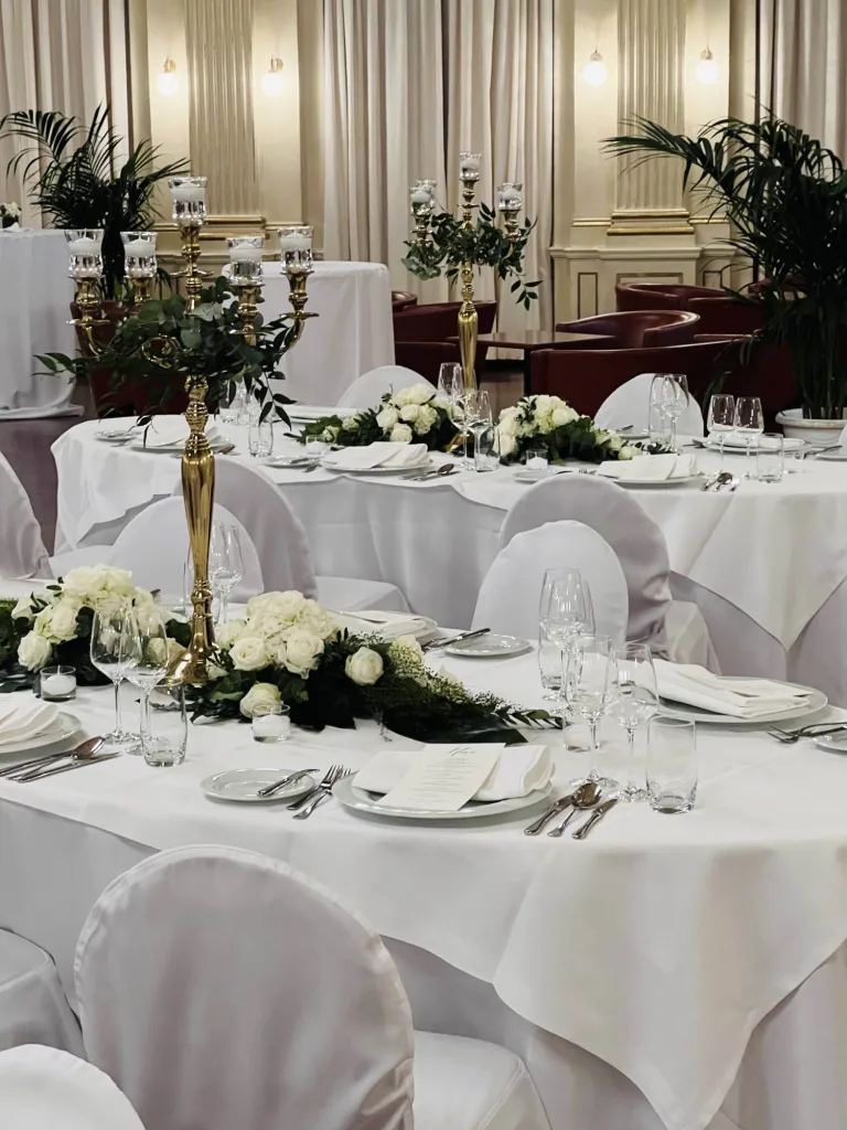 Hochzeitstafel mit weißen Rosengestecken, goldenen Kerzenleuchtern und Eukalyptusgrün