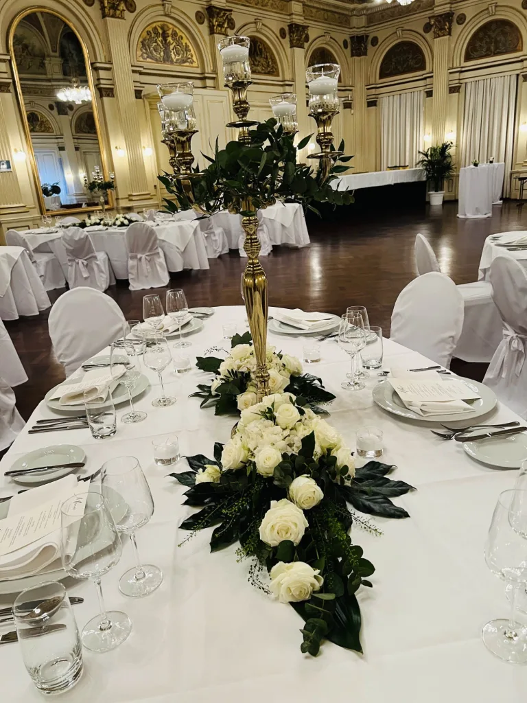 Runder Hochzeitstisch mit langem Gesteck aus weißen Rosen und einem goldenen Kerzenleuchter